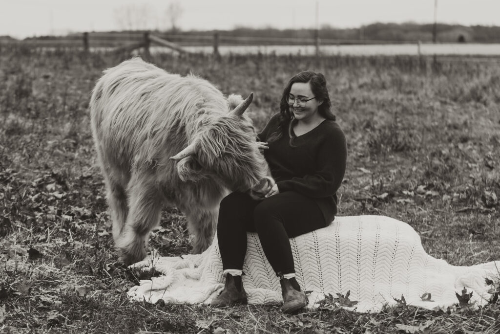 photo of photographer Callie sitting on a hay bale next to a highland cow. 